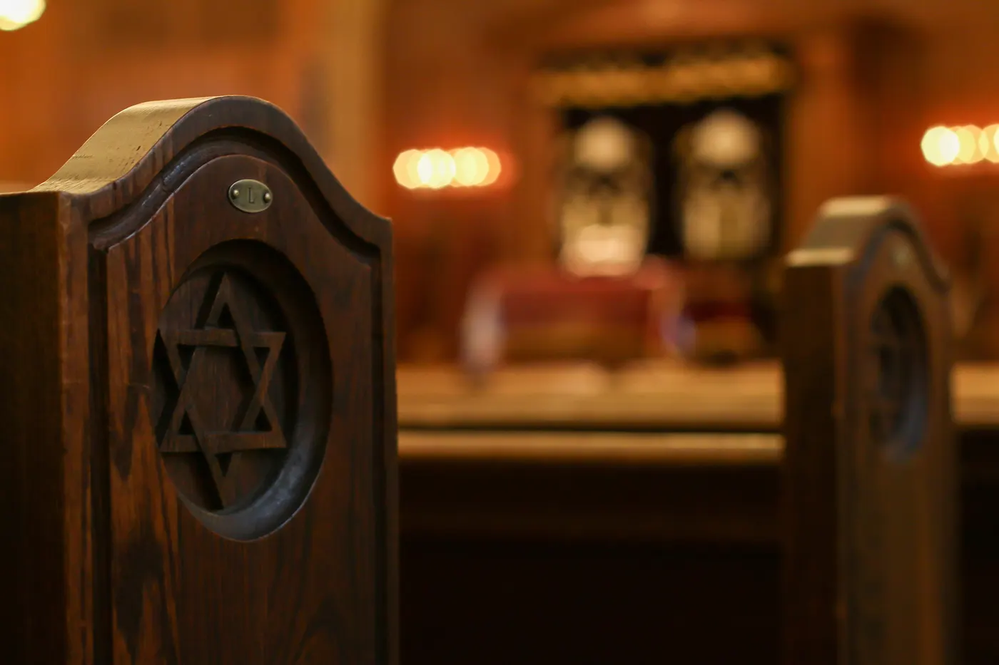 A wooden pew end carved with a Magen David, the Aron Kodesh glowing behind it